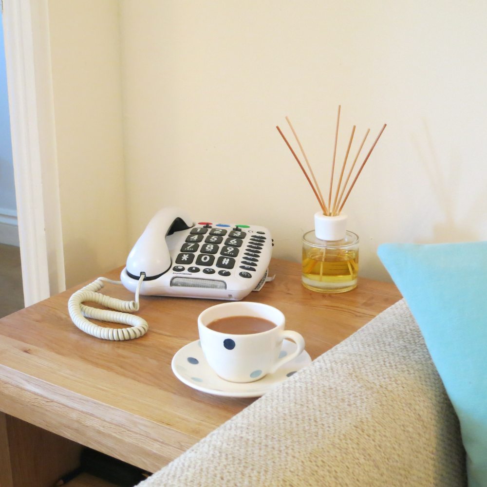Corded phone with large buttons, a cup of tea and a diffuser on a side table