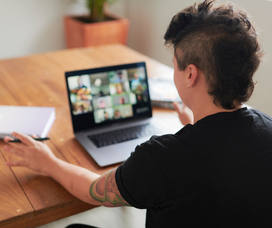 Person sitting at a table looking at a laptop with a group online meeting on screen