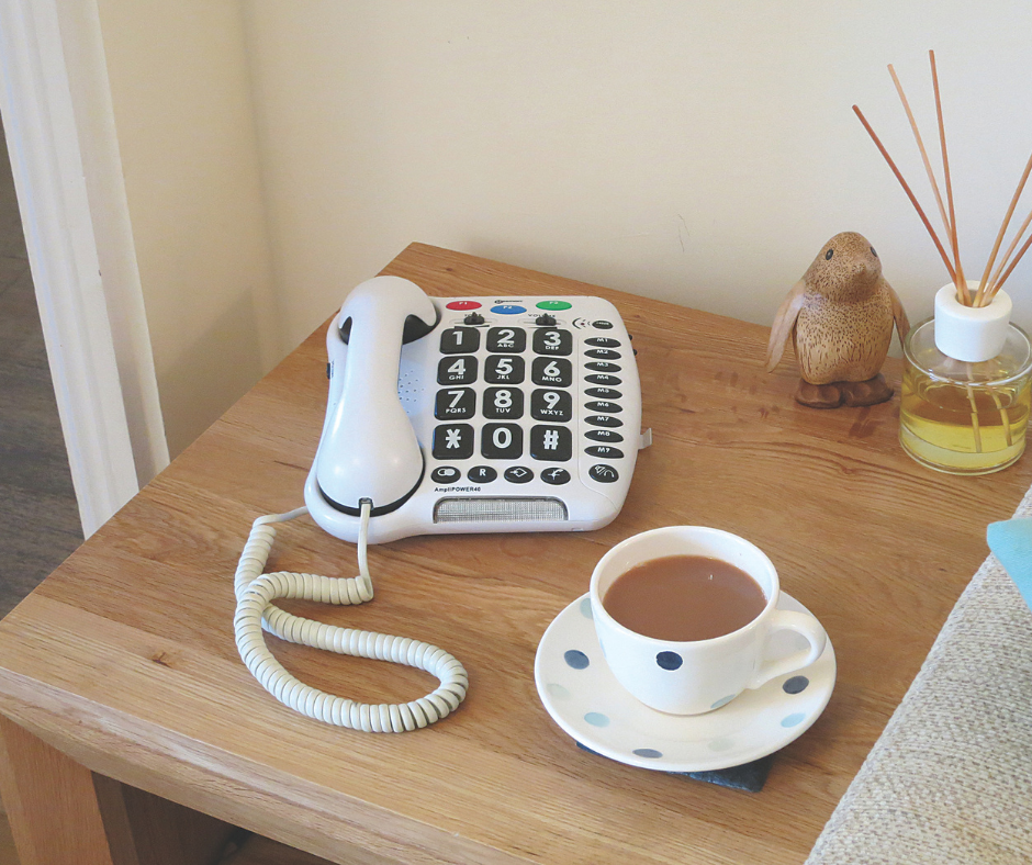 A telephone and tea cup and saucer with tea on a side table in a living room