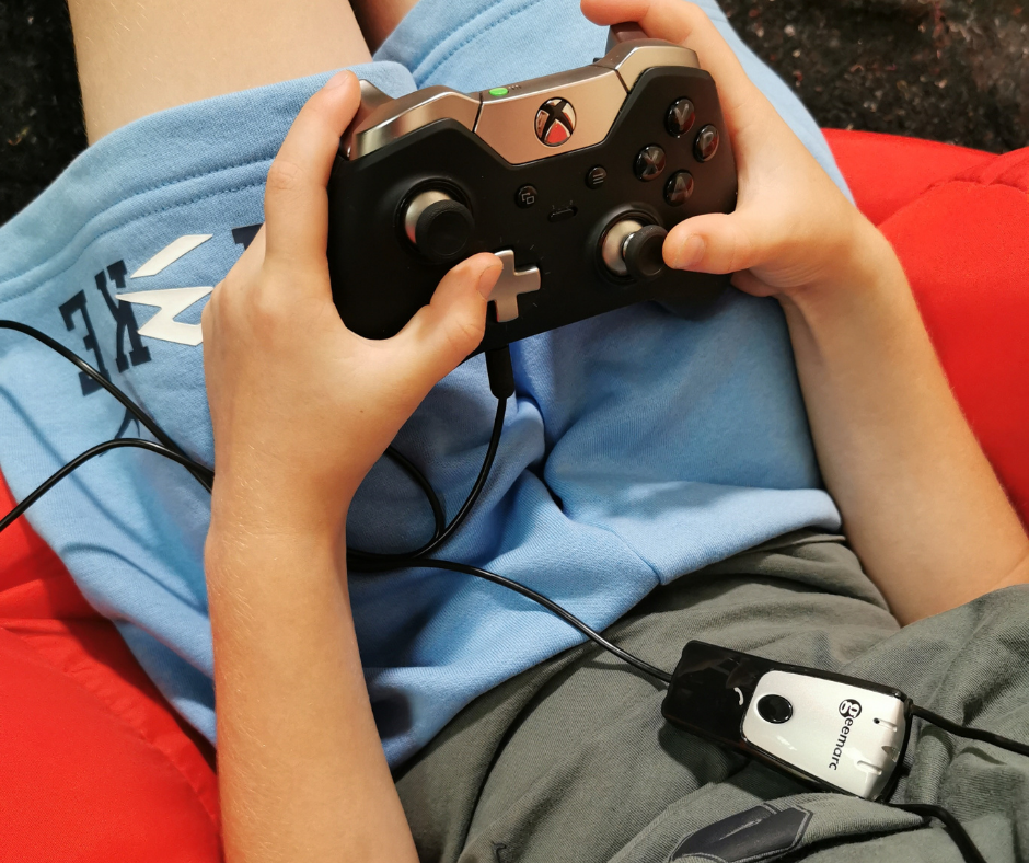 Child holding an Xbox games console controller with a Geemarc neckloop plugged into it