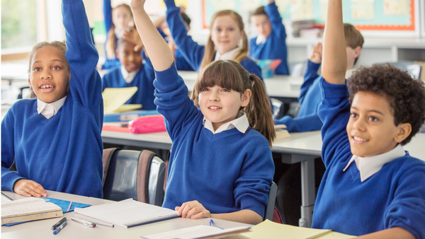 Students in a classroom wearing blue school uniform with their hands up in the air