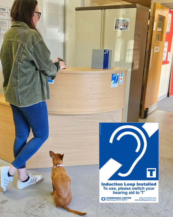 person and their dog waiting in a building reception area with a induction loop sign visible on the reception desk