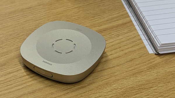 Phonak Roger Table Mic III sitting on a work desk placed alongside a notepad